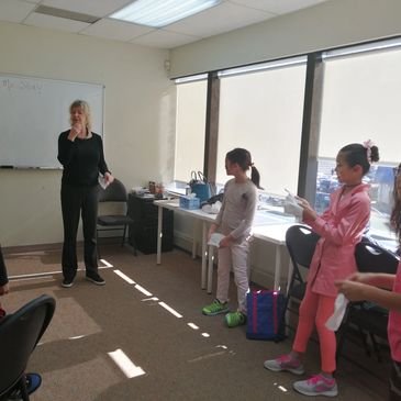 A teacher standing at the whiteboard in a bright classroom while students work at their desks